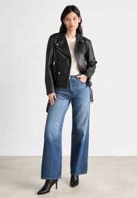 Must musta biker-jakk nahast, millel on tõmblukuga taskud, kantud Kerget särgi kohal, kombineeritud laia säärega siniste teksade ja mustade terava ninaga kontsadega.