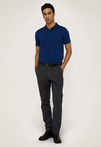 Polo en coton bleu marine avec un col à boutons, associé à un pantalon fuselé gris foncé et des bottines noires.
