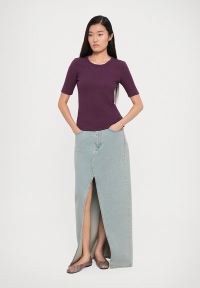 Purple fitted t-shirt with short sleeves, paired with a light blue denim maxi skirt featuring a front slit. Worn with striped flat shoes.