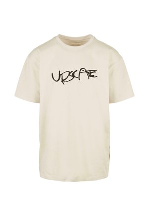 T-shirt en coton couleur crème à manches courtes et col rond, arborant un design graphique en texte noir "UPSCALE" sur le devant.
