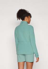 Veste en polaire bleu clair avec un col montant, des coutures plates et un logo discret dans le dos, assortie à un short léger.