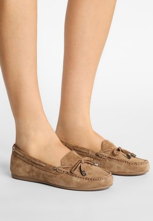 Zapatos estilo mocasín de ante en marrón claro, con cordones decorativos, acentos metálicos y una suela plana y flexible.