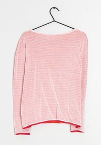 Lichtroze blouse met lange mouwen en subtiele horizontale strepen, rode afwerking bij de mouwen en onderkant, hangend aan een zwarte draadhanger tegen een witte achtergrond.