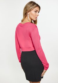 Feszes, hosszú ujjú, élénk rózsaszín pulóver bordás mandzsettával, fekete miniszoknya fölött. Simább textúra, cropped kialakítással.