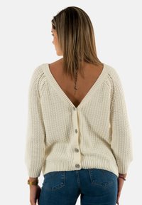 Pull en crème tricoté avec un dos en V profond, des manches trois-quarts et une fermeture à boutons dans le dos, avec des détails en tissu texturé.