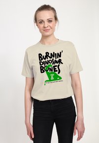 Crème-kleurig katoenen t-shirt met zwart en groene grafische tekst: "BURNIN' DINOSAUR BONES" met een druipend groen accent.