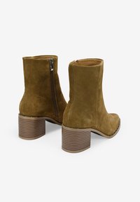 Botas de tobillo de ante marrón con punta redondeada, cremallera lateral y un tacón apilado y texturizado con un diseño estriado.