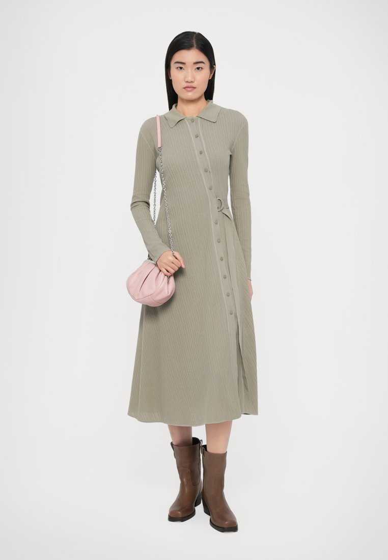 Robe côtelée à manches longues avec boutons, en vert olive, dotée d'un col et d'une ceinture. Assortie à un sac à main rose et des bottines marron.