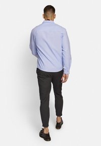 Lichtblauw overhemd met lange mouwen, gecombineerd met donkerblauwe pantalon met fijne strepen en bruine schoenen, gezien van achteren.