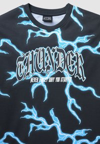 Czarna koszulka z niebieskim wzorem błyskawic, z napisem "THUNDER" w pogrubionym białym tekście i "NIGDY NIE ZAPOMNIJ DLACZEGO ZACZĄŁEŚ" poniżej.