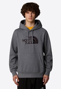 Sudadera gris de mezcla de algodón, con un bolsillo frontal, capucha con cordón y un logo oscuro en el pecho. Puños y dobladillo acanalados.