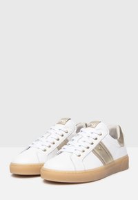 White sneakers with gold accents, featuring lace-up closure, smooth leather upper, and a textured gum rubber sole.