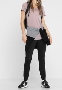 Ljusrosa t-shirt med kort ärm, grå lagertröja knuten runt midjan, svarta cargo-byxor med fickor, i kombination med svarta träningsskor.