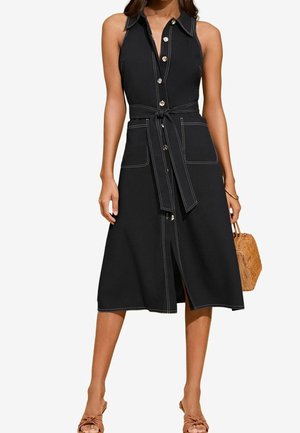Vestido negro de botones con cintura ajustable, detalles de bolsillo y costuras en blanco que contrastan. Largo midi fluido con una abertura frontal.