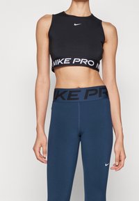 Černý zkrácený sportovní top s pruhem "NIKE PRO" a námořnickými legínami s bílým logem. Hladká, elastická látka, navržená pro aktivní nošení.