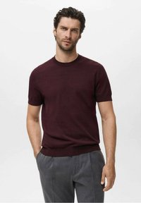 Pull en maille bordeaux à manches courtes avec un col rond et des poignets côtelés, associé à un pantalon gris ajusté. Texture lisse, design minimaliste.