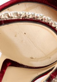 Gros plan de l'intérieur d'une chaussure beige avec bordure en velours rouge et décoration en strass le long du bord.