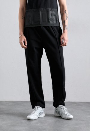 Sort ærmeløs top med glansfuld panel, der har præget bogstaver, parret med sorte plisserede joggers og sølvfarvede sneakers.