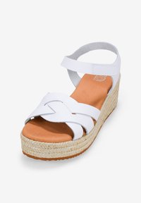 Las sandalias de cuña blancas presentan una plataforma trenzada, un diseño de correas cruzadas, una plantilla beige y una correa de tobillo ajustable para un ajuste seguro.