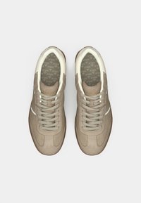 O pereche de pantofi sport bej din suede, cu detalii albe și șireturi albe, logo-ul "REPLAY" pe limbă și branțuri imprimate, văzuți din perspectiva de sus.