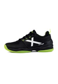Zapatilla deportiva negra con un logotipo blanco en forma de "X", detalles verdes, parte superior de malla perforada, suela texturizada y una lengüeta prominente en el talón para facilitar su uso.