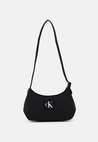 Borsa a spalla nera in nylon con una forma curva, tracolla intrecciata e un logo del marchio prominente su una toppa quadrata. Texture liscia, design minimale.