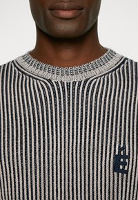 Strickpullover in marineblau und cremefarbenen Streifen; verfügt über einen runden Halsausschnitt und ein gesticktes Logo auf der Brust. Strukturierter Stoff mit geripptem Design.