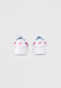 Baltie Nike Air sneakers izceļas ar gludu ādas virspusi un rozā akcentiem. Papēdis ir aprīkots ar noapaļotu logotipu un fakturētu zoli, kas nodrošina labāku saķeri.