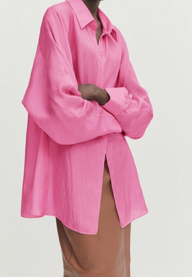 Roze blouse met lange mouwen, knopen aan de voorkant, relaxte pasvorm en lichtdoorzichtige stof. Voorzien van een klassieke kraag en verlaagde schouders.