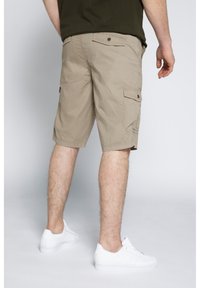 Pantaloni cargo beige con tasche laterali, realizzati in tessuto leggero. Indossati con sneakers bianche, che mostrano uno stile informale.