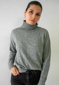 Grijze gebreide coltrui met ribbelmanchetten en verticale kabelpatronen, gecombineerd met donkere jeans. Soepele textuur, relaxte pasvorm.