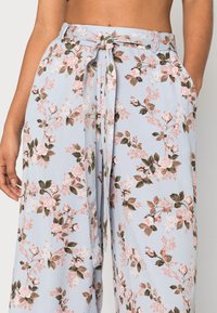 Light blue wide-leg pants made from fabric featuring a pink floral pattern. Includes a tie waistband and side pockets for added functionality.