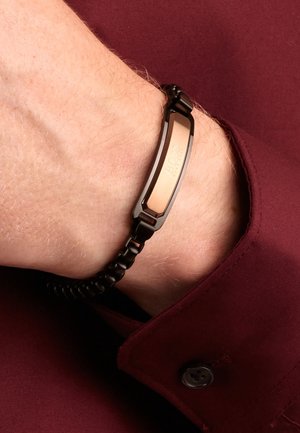 Zwart metalen schakelenarmband met een roségouden plaatje gegraveerd met BOSS, gedragen om een pols boven een bordeauxrode overhemdmanchet met een knoop.
