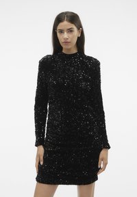 Juoda sequin suknelė su ilgomis rankovėmis ir aukštu iškirpimu; aptempta silueto forma su raukšlėmis apatinėje dalyje; blizgi tekstūra dėl persidengiančių sequinų.