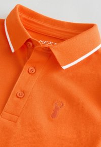 Polo shirt orange avec un tissu texturé, doté d'un col à rayures blanches et de trois boutons. Comprend un subtil logo de homard brodé.