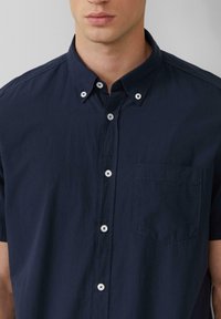 Camisa de boton corto de manga corta en color navy con cuello, bolsillo en el pecho y botones blancos. La tela tiene una textura suave y un drapeado ligero.