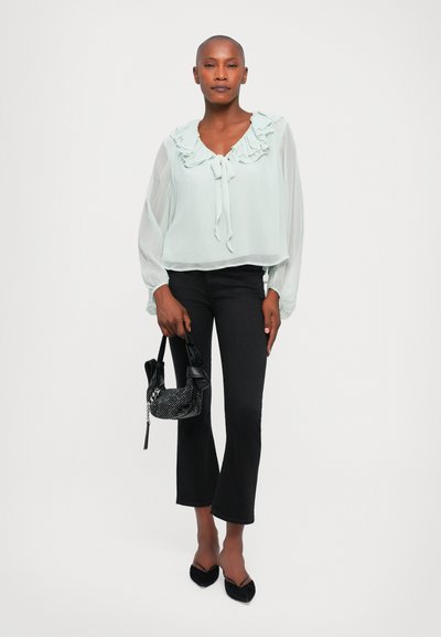 Light mint blouse with ruffled neckline, flowing long sleeves, paired with black flared jeans and a black embellished handbag.