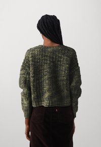 Pull vert texturé à la coupe ample, col rond et longueur raccourcie. La surface présente un motif tricoté, porté avec une jupe foncée.