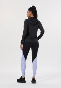 Schwarzes langärmeliges Hoodietop kombiniert mit schwarzen und helllila gemusterten Leggings. Die Leggings haben ein Color-Block-Design und eine strukturierte Stoffqualität.