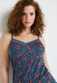 Camicetta floreale blu con dettagli rossi, caratterizzata da spalline sottili e cuciture decorative lungo il colletto, realizzata in tessuto morbido e traspirante.