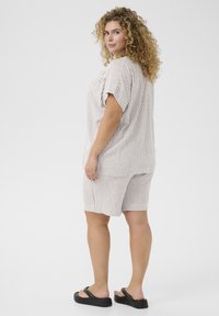 Ribade loungewear komplekt beež ja valge, koos laia lühikeste varrukatega toppi ja sobivate lühikeste pükstega, millel on elastne vöökoht. Mustad platvormsandaalid.