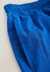 Shorts à taille élastique bleue avec poche latérale et motif géométrique ton sur ton sur le tissu.