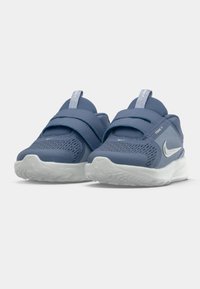 Blå atletiska skor med mesh-överdel, kardborreband och vit sula; har Nike-logotypen på sidan, rund tå och vadderad krage.
