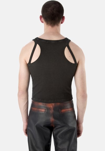 Homme portant un haut noir sans manches avec découpes et un pantalon en cuir noir avec des accents rougeâtres, vu de dos sur fond blanc.