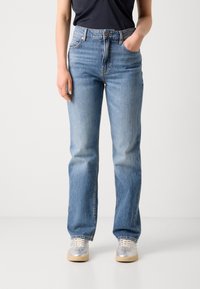 Lichtblauwe denim jeans met een rechte pijp, hoge taille, met vervaging op de bovenbenen en zijzakken. Gecombineerd met grijze sneakers.