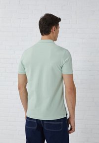 Mint green polo shirt with short sleeves and a collar, paired with dark blue denim jeans. Fabric appears smooth with side slits.