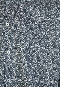 Tessuto bianco e nero con un denso motivo di foglie di monstera e bottoni bianchi visibili su una camicia abbottonata.