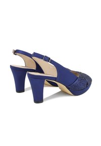 Scarpe con tacco slingback blu navy con una texture lucida, con punta aperta e decorate con strass sul davanti. Tacco spesso per stabilità.
