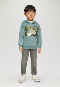 Turquoise hoodie met gouden bedrukt tekst "SPACE STAR MOON," gecombineerd met grijze jeans en witte sneakers met grijze accenten.