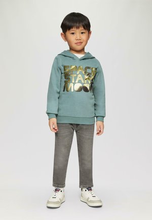 Turquoise hoodie met gouden bedrukt tekst "SPACE STAR MOON," gecombineerd met grijze jeans en witte sneakers met grijze accenten.